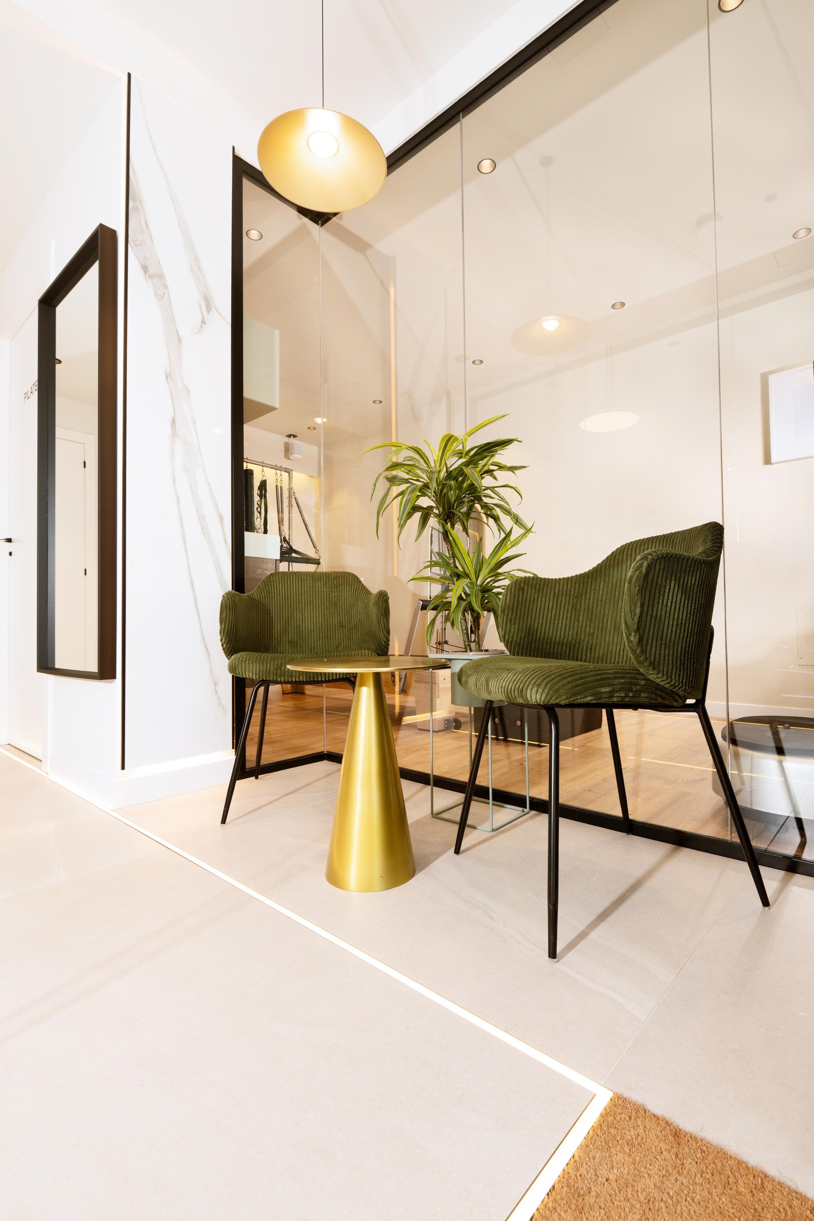 Zona d'espera i lounge de benvinguda al Local 2 de Physio Wellness by Marshall amb butaques de vellut verd oliva i taula daurada.