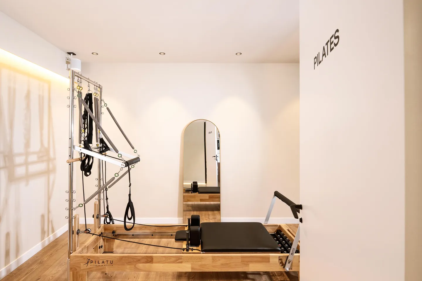 Estudio de Pilates Reformer con torre de madera noble y espejo de arco en Physio Wellness Sitges