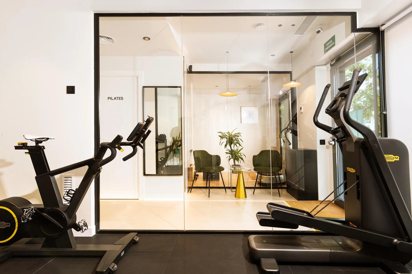 Zona cardiovascular Technogym amb bicicleta i el·líptica, terra tècnic i mampara de vidre cap a la zona de descans i Pilates.